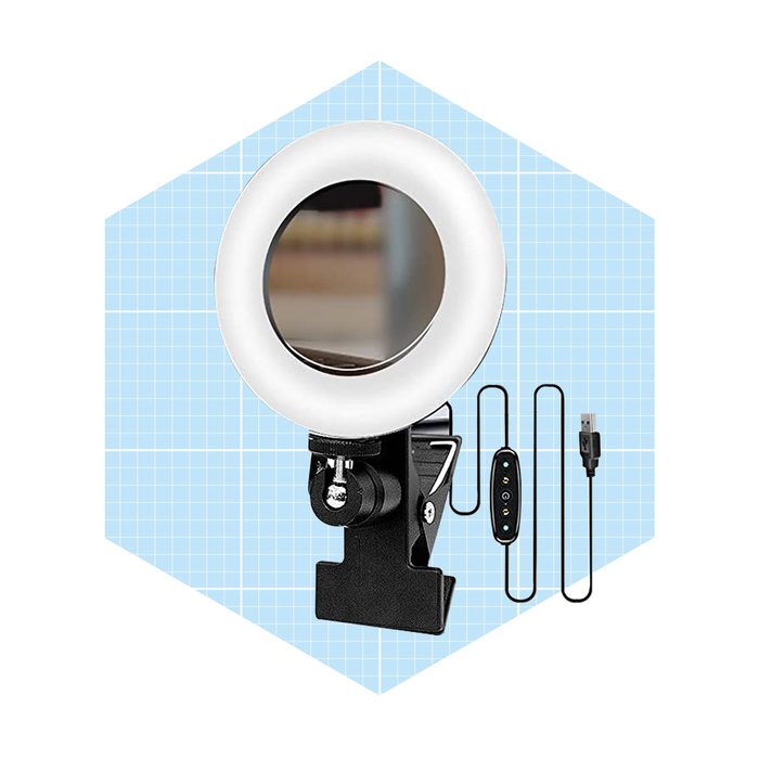 A circular ring light with a mirror is mounted on a clamp. It is accompanied by a USB cable and a control device, set against a light blue grid.