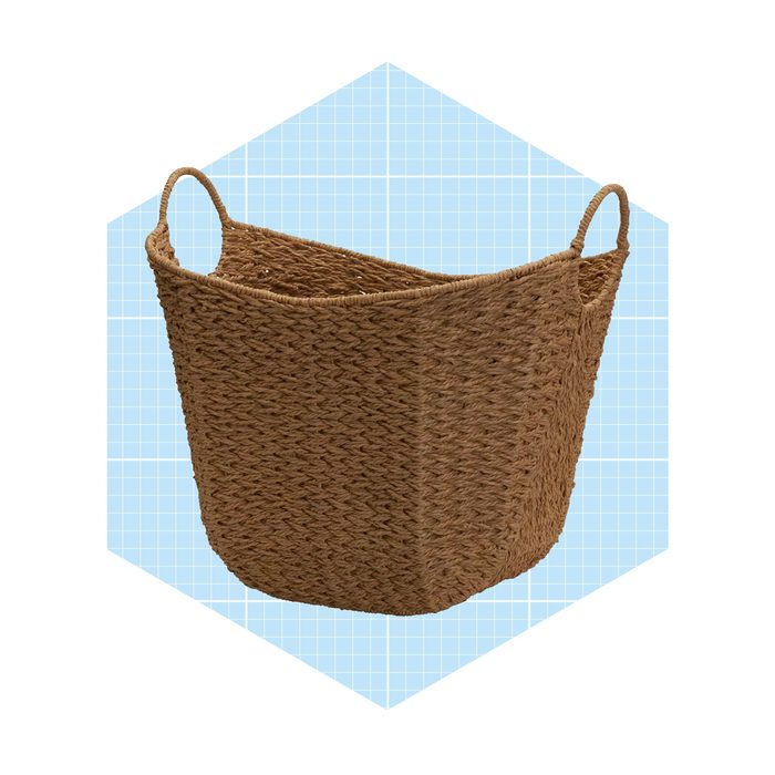 A woven basket stands upright with two handles, set against a light blue grid background, suggesting a contemporary, organized space.
