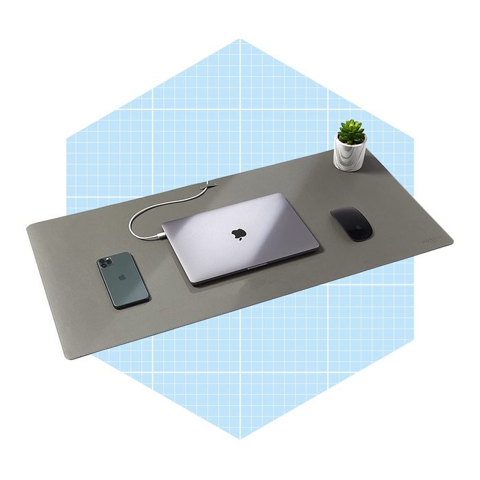 A laptop, phone, and mouse sit on a sleek desk mat, connected by a charging cable, with a small plant in a pot nearby.