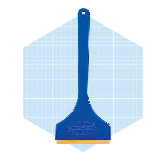 A blue scraper tool with a flat edge and handle rests against a light blue grid-patterned background, indicating a measuring or crafting context.