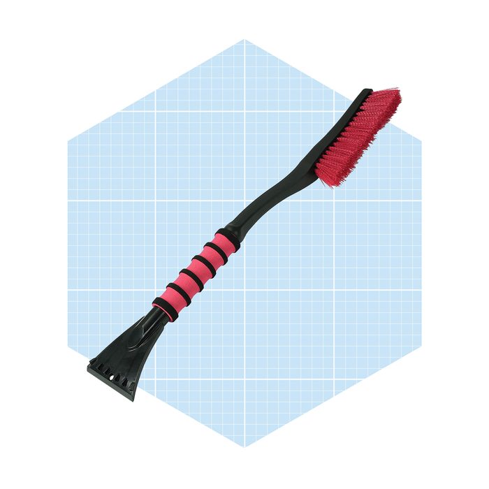 A black and pink ice scraper and brush lies horizontally, designed for removing snow and ice from vehicle surfaces, set against a light blue grid background.