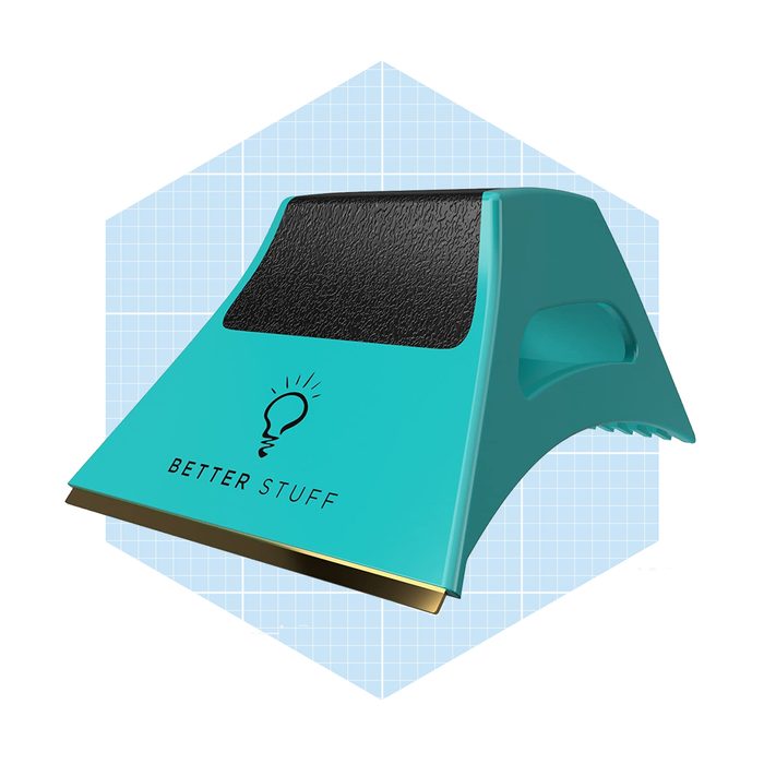 A teal plastic scraper with a black rubber grip and a gold metal edge rests against a light blue grid-patterned background, labeled 