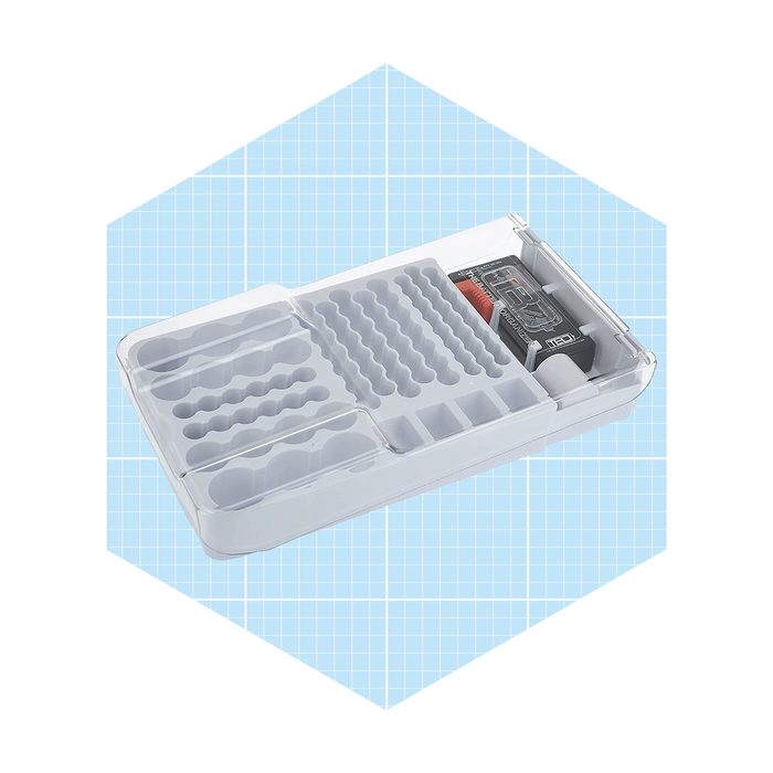 A clear storage box with various compartments holds small items, including a battery pack, against a light blue grid background.