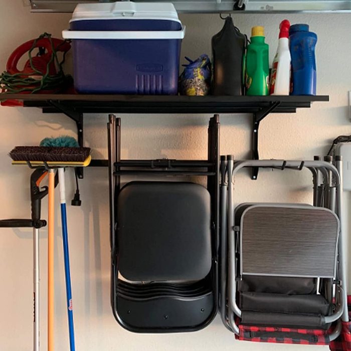 A black folding chair hangs on a wall beside a shelf holding a cooler and various cleaning supplies, with mops and brushes leaning against the wall.