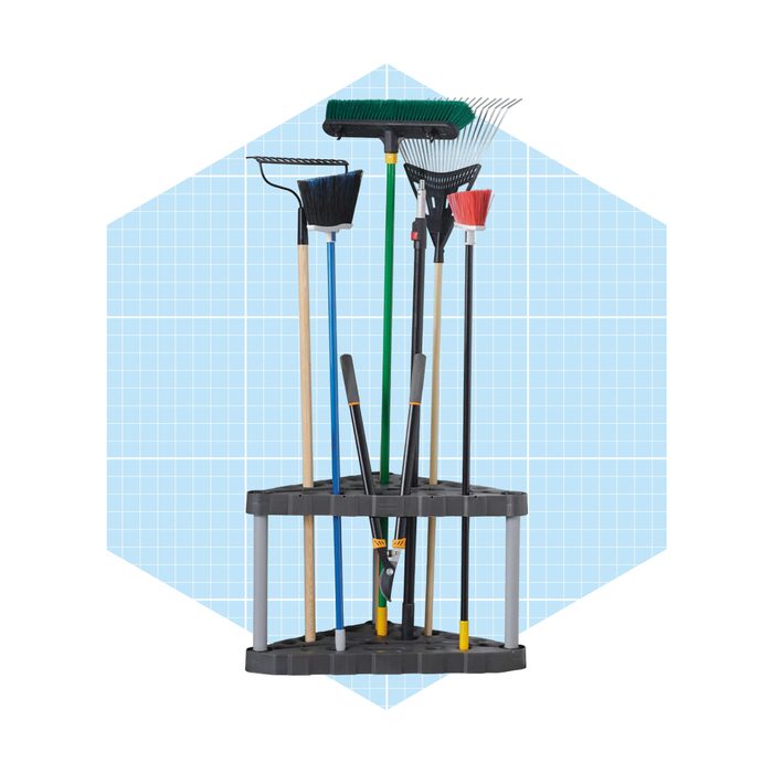 A storage rack holds various garden tools, including brooms and rakes, organized upright against a light blue grid background.