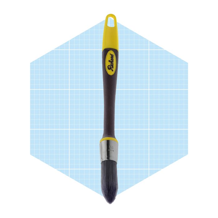 A paintbrush with a yellow handle applies color against a light blue grid background, showcasing its bristles and metal ferrule clearly.