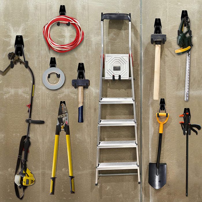 A variety of tools, including a ladder and cutting equipment, hang on wall mounts in a workshop setting, organized for easy access and use.