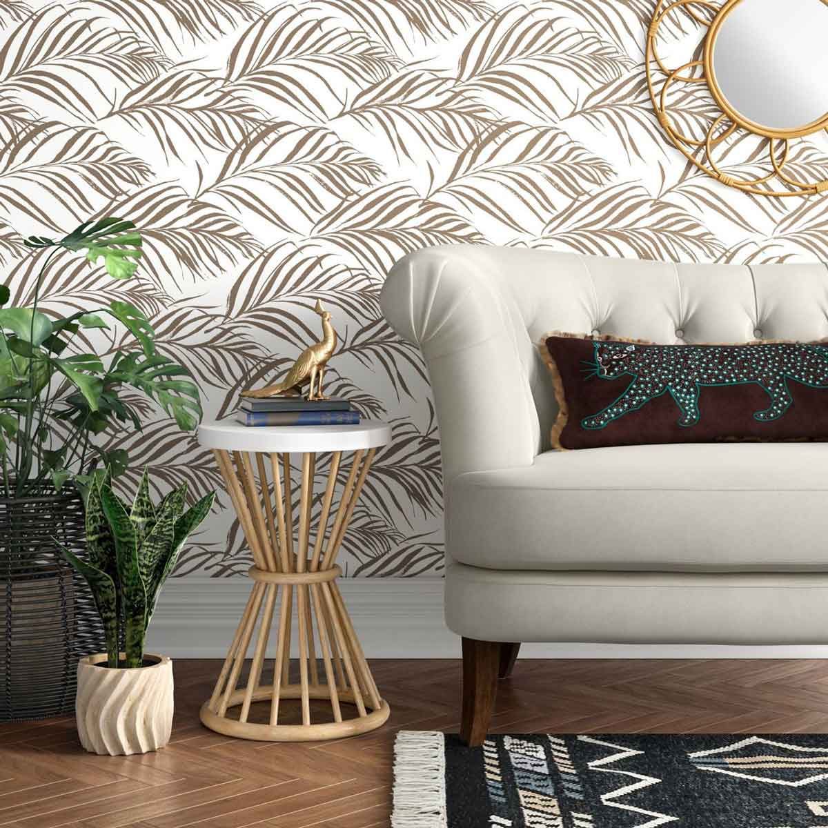 A beige sofa sits against a leaf-patterned wall, beside a plant and a table topped with decor, creating a cozy, stylish space.