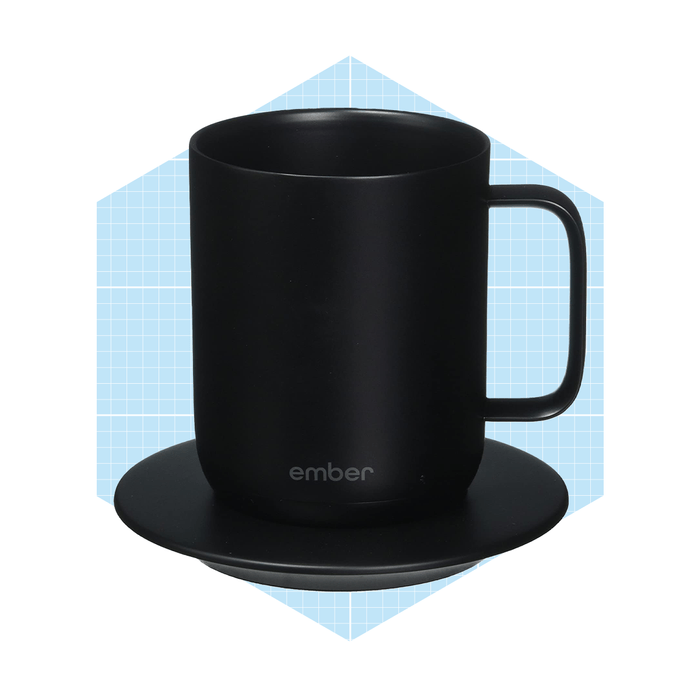 A black mug rests on a round coaster, holding heat. The background features a light blue grid pattern, enhancing the modern aesthetic.
