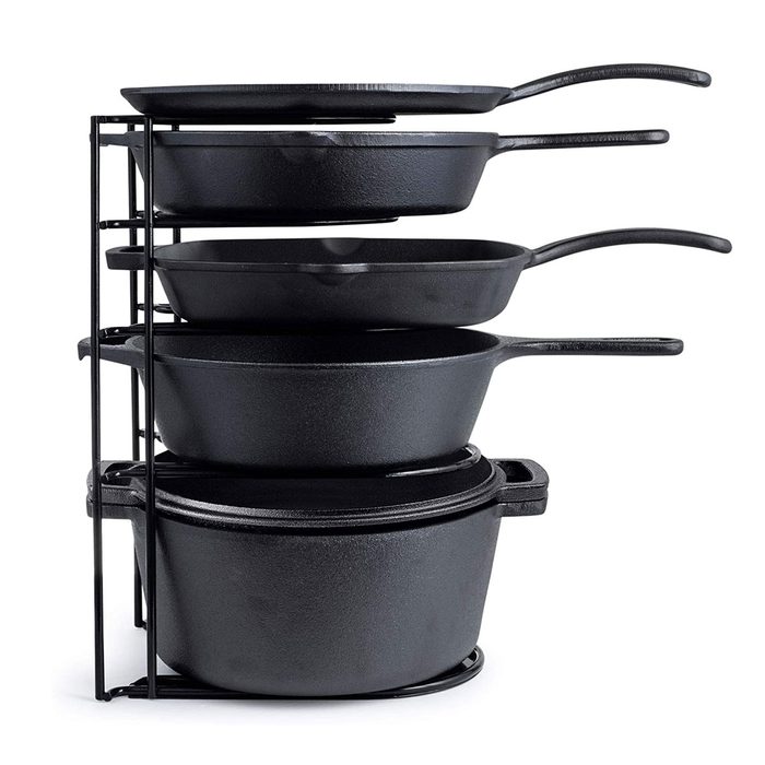 A stack of four black cast iron cookware pieces sits vertically on a black metal rack, organized for efficient storage or display.