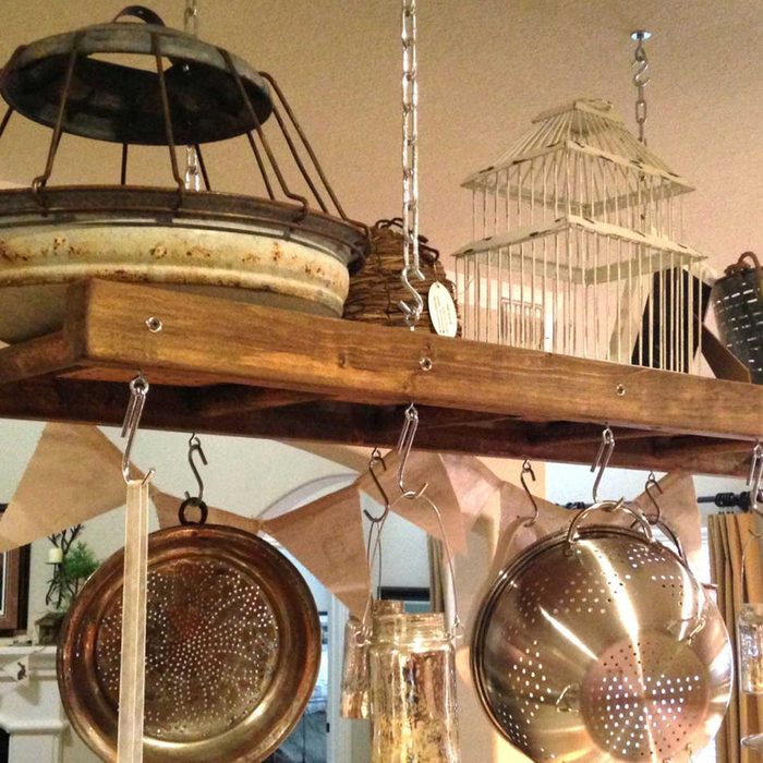 Hanging kitchen items, including pots and colanders, rest on a wooden shelf. Decorative elements, like a birdcage and banners, create a cozy ambiance indoors.