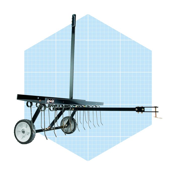 A garden rake with wheels is positioned upright, ready for use. Its metal tines are designed for soil aeration, set against a light blue grid background.