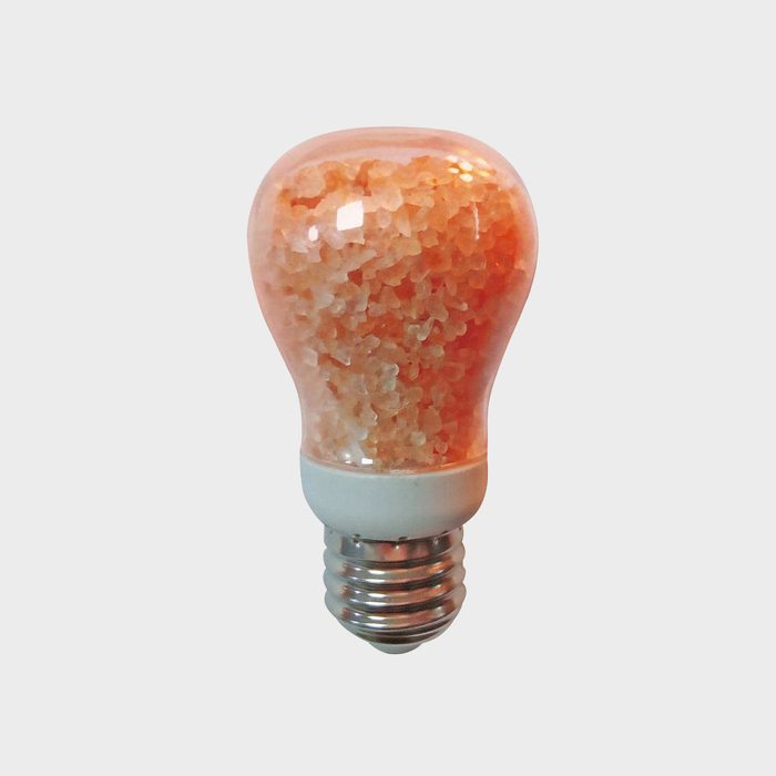 A light bulb filled with pinkish salt sits upright, showcasing its textured interior, while the base is designed for standard light socket insertion.