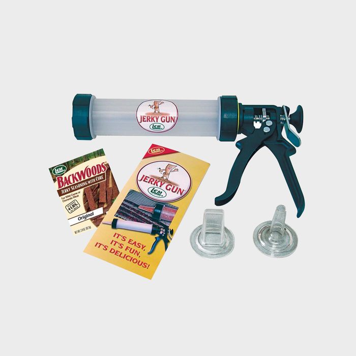 A jerky gun sits alongside seasoning packets and attachments, indicating preparation for making jerky in a home kitchen environment.