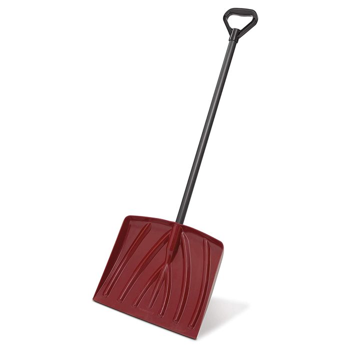 A red snow shovel stands upright with a black handle, designed for lifting and moving snow, typically used in cold, snowy environments.