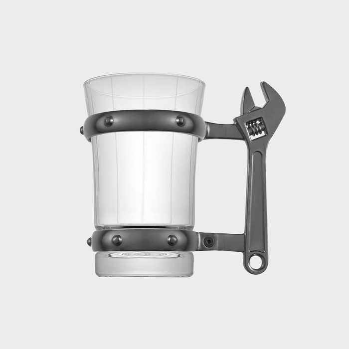 A clear glass mug with a metallic wrench-shaped handle rests on a flat surface against a neutral background.