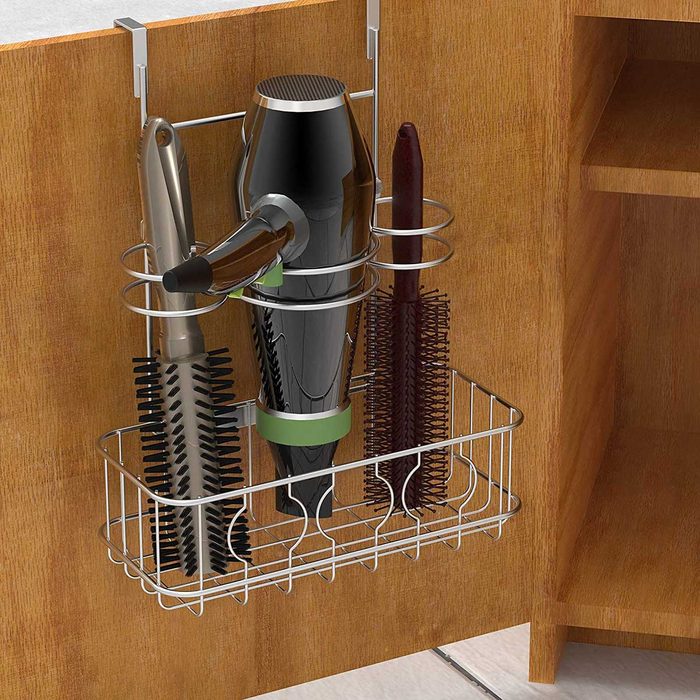 A metal organizer hangs under a counter, holding a hair dryer, two combs, and a brush, set against a wooden cabinet backdrop.