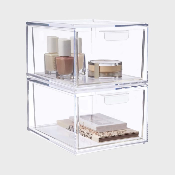 A clear acrylic storage box holds nail polish, cream, and books, organized into two stacked compartments, set against a neutral background.