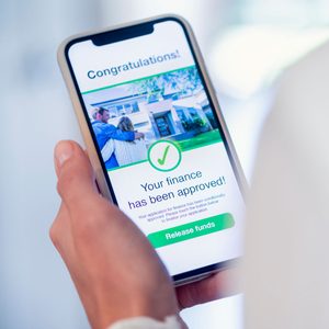 A smartphone displays a finance approval notification, featuring a checkmark, congratulatory message, and options to release funds, held by a person in a light setting.