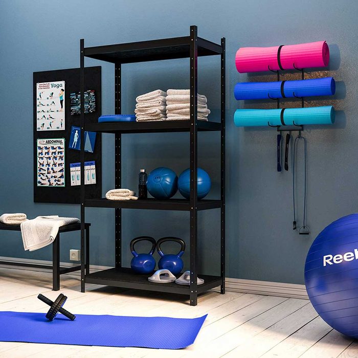 A black shelf displays towels and fitness equipment in a workout space, featuring blue exercise balls, mats, and kettlebells against a blue wall.