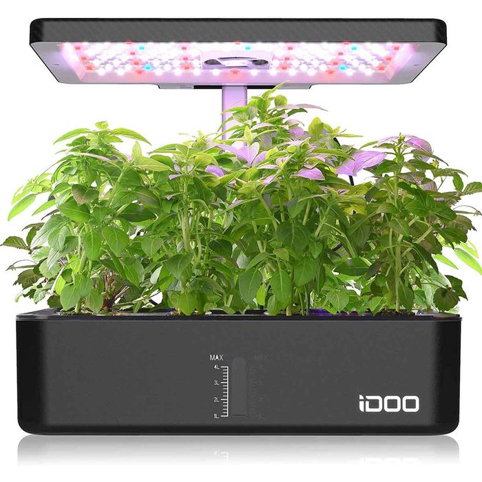 A hydroponic plant growing system featuring vibrant green plants supported by a LED light panel above, set against a simple white background.