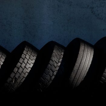 A series of six car tires are arranged in a curved line, showcasing varied tread patterns against a dark background, highlighting texture and shape.