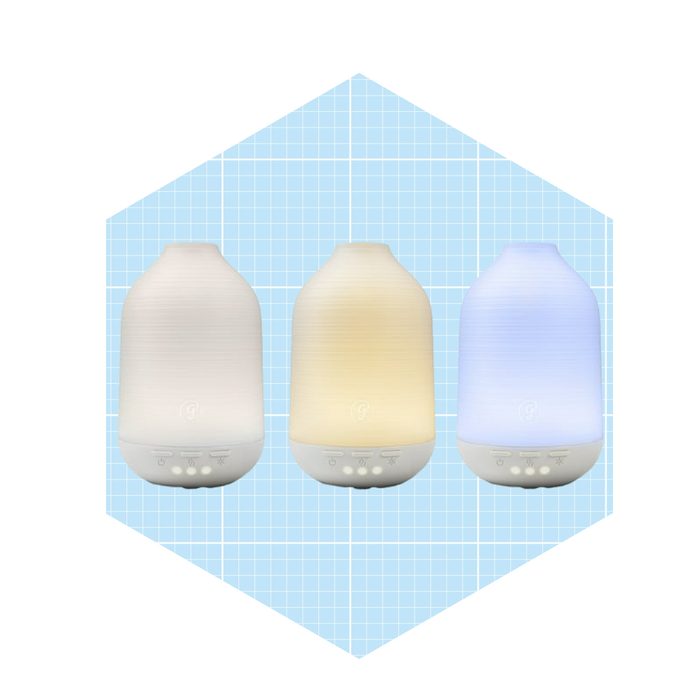 Three essential oil diffusers emit soft, adjustable light, arranged in a row on a light blue grid background, promoting relaxation and ambiance.