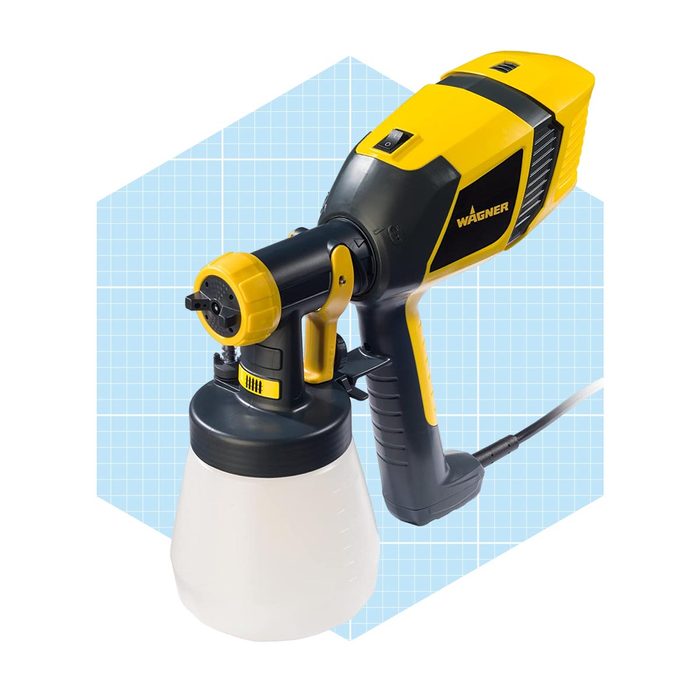 A paint sprayer with a black and yellow design rests on a light blue grid background, ready for use in painting tasks.