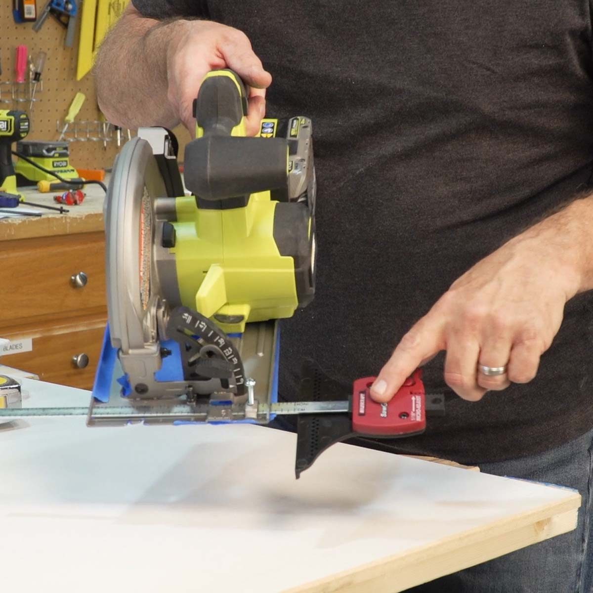 A person holds a power saw, measuring the wood with a tool on a workbench surrounded by various tools and materials.