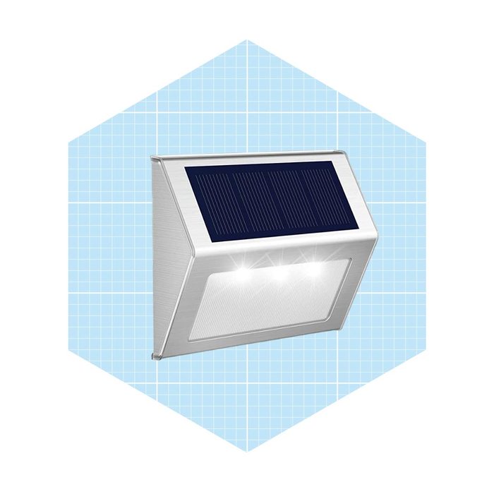 A solar-powered wall light is mounted, illuminating with three bright LEDs against a light blue grid background.
