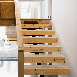 A wooden staircase ascends, featuring open treads and a handrail, situated in a well-lit, modern interior with large glass windows.