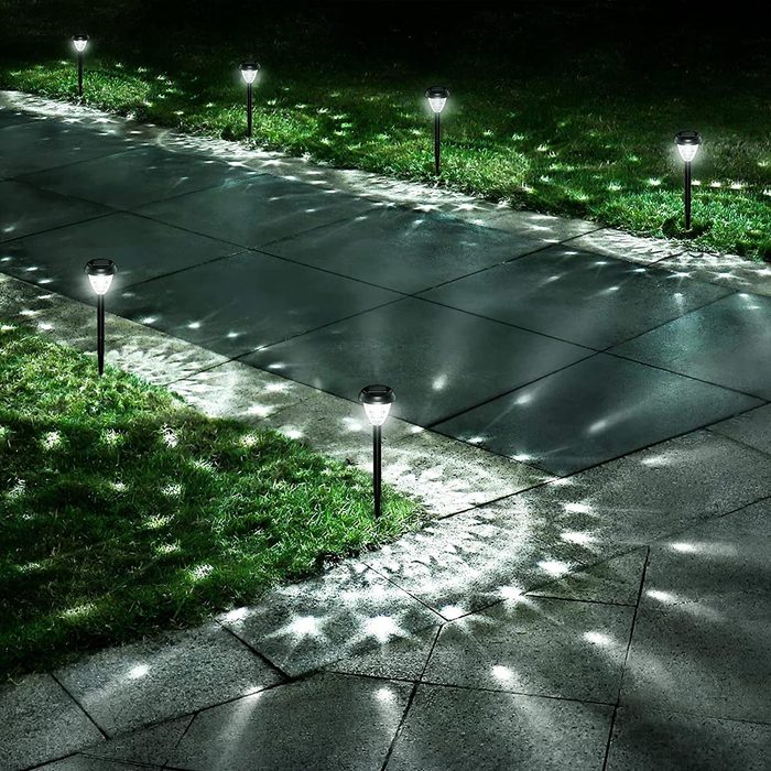 Garden path illuminated by solar lights, casting star-like reflections on the pavement and grass in a serene nighttime setting.