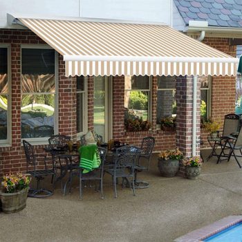 A striped awning extends over a patio dining area with metal furniture, surrounded by potted flowers, against a brick wall by a pool.