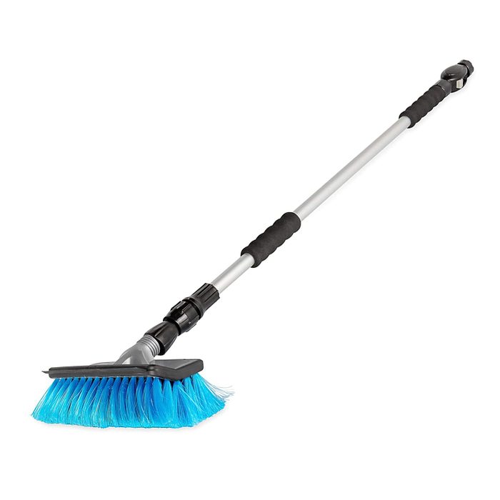 A long-handled broom with a blue bristle head is positioned upright, ready for sweeping. The handle is metallic with black rubber grips for comfort.