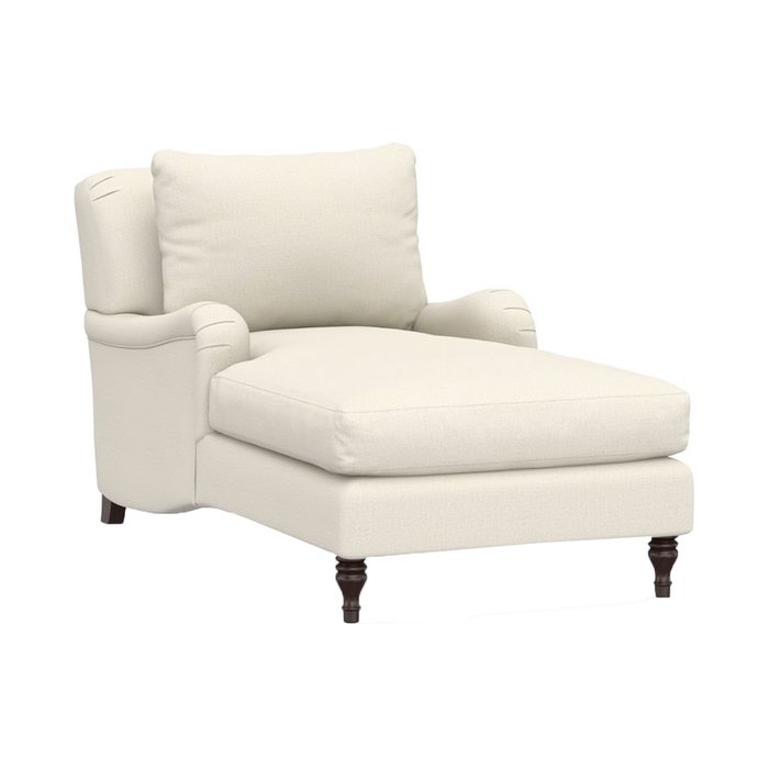 A cream-colored chaise lounge rests on dark wooden legs, featuring a plush cushion and supportive back, ideal for relaxation in a cozy setting.