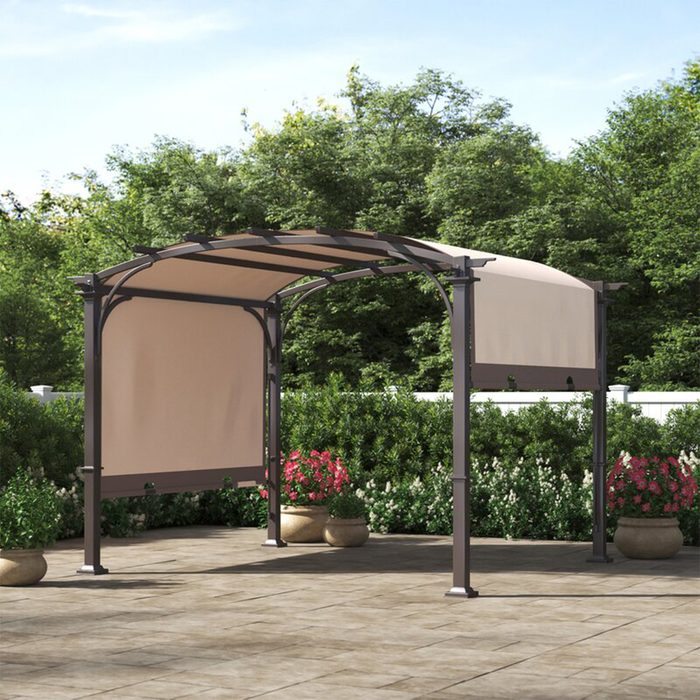 A metal pergola stands on a patio, featuring a fabric canopy. Surrounding greenery and flower pots create a tranquil outdoor setting.