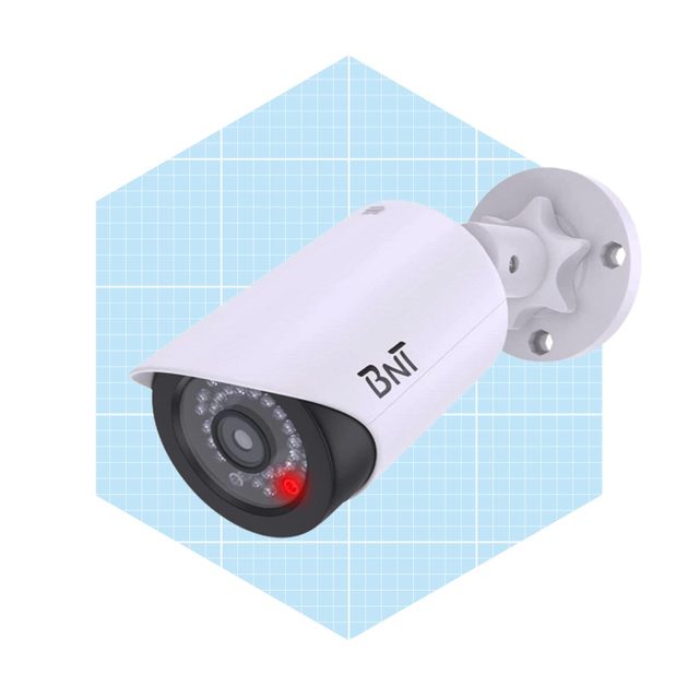 A security camera is mounted on a wall, actively monitoring the area, with a red indicator light on, set against a light blue grid background.