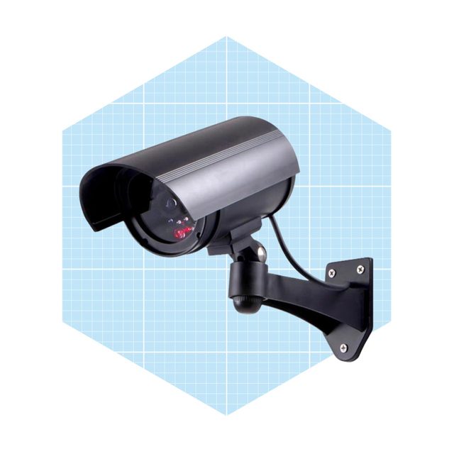 A security camera is mounted on a wall, monitoring its surroundings. It features a protective cover and a visible recording light against a light blue grid background.