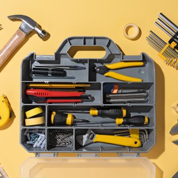 A toolbox is organized with various tools, including a hammer, screwdrivers, and pliers, placed on a yellow surface.