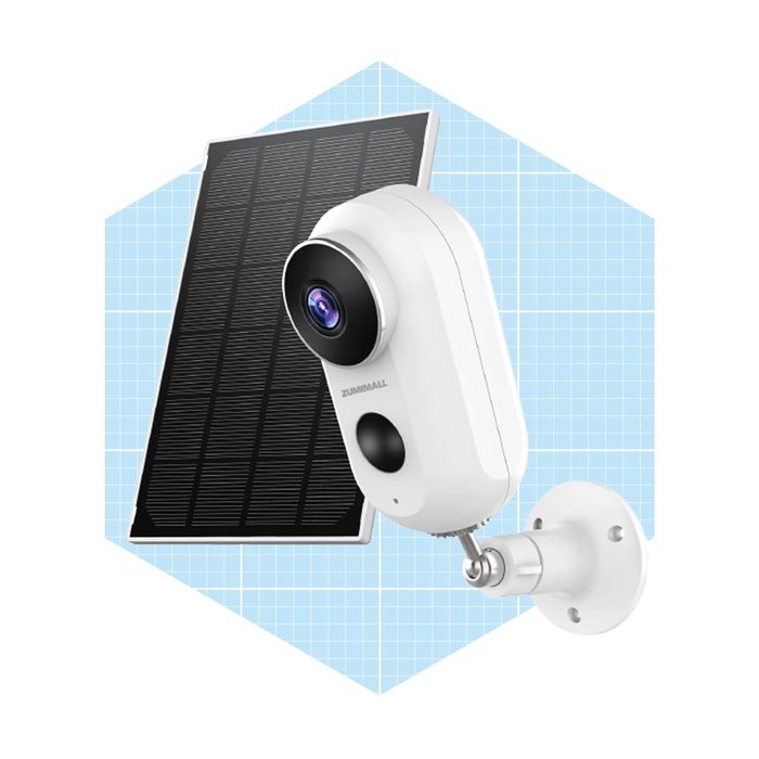 A white security camera attaches to a wall while connected to a solar panel, designed for outdoor surveillance in a grid-patterned blue background.