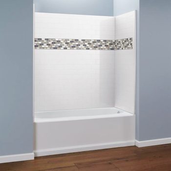 A bathtub is installed in a simple bathroom, surrounded by white tiled walls featuring a decorative mosaic strip, with blue-painted walls and wooden flooring.