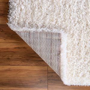 A fluffy white rug partially rolled back reveals a textured tan underside, situated on a wooden floor, creating a cozy, inviting atmosphere.