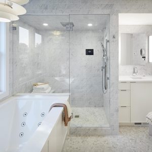 A freestanding bathtub sits beside a glass shower in a modern bathroom, featuring marble tiles, a sleek sink, and ample natural light from a window.