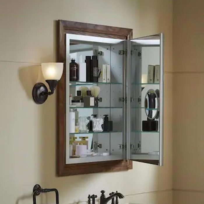 A mirrored medicine cabinet is open, displaying various bottles and containers inside, beside a wall-mounted light fixture in a bathroom setting.