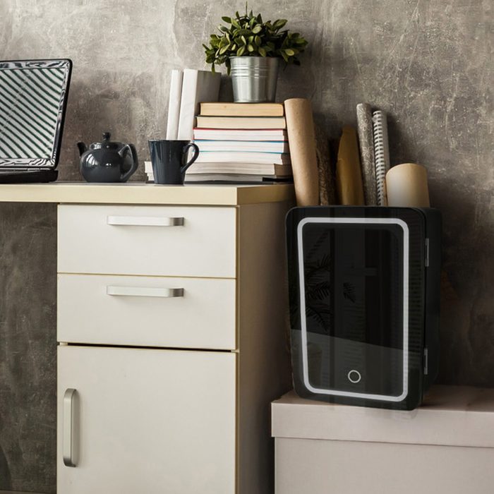 Interior of a modern home office next to a big window. Light wood desk with organized set up of books, office supplies and laptop with some room decor around it