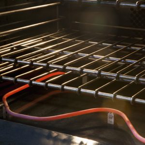Metal oven racks sit above a glowing red heating element, illuminated by soft light with a dark background, suggesting a warm baking environment.