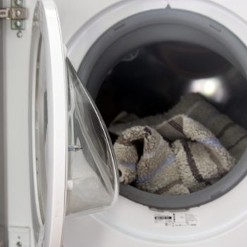 A washing machine door is open, revealing a striped towel inside, ready for a wash cycle in a clean, well-lit laundry space.