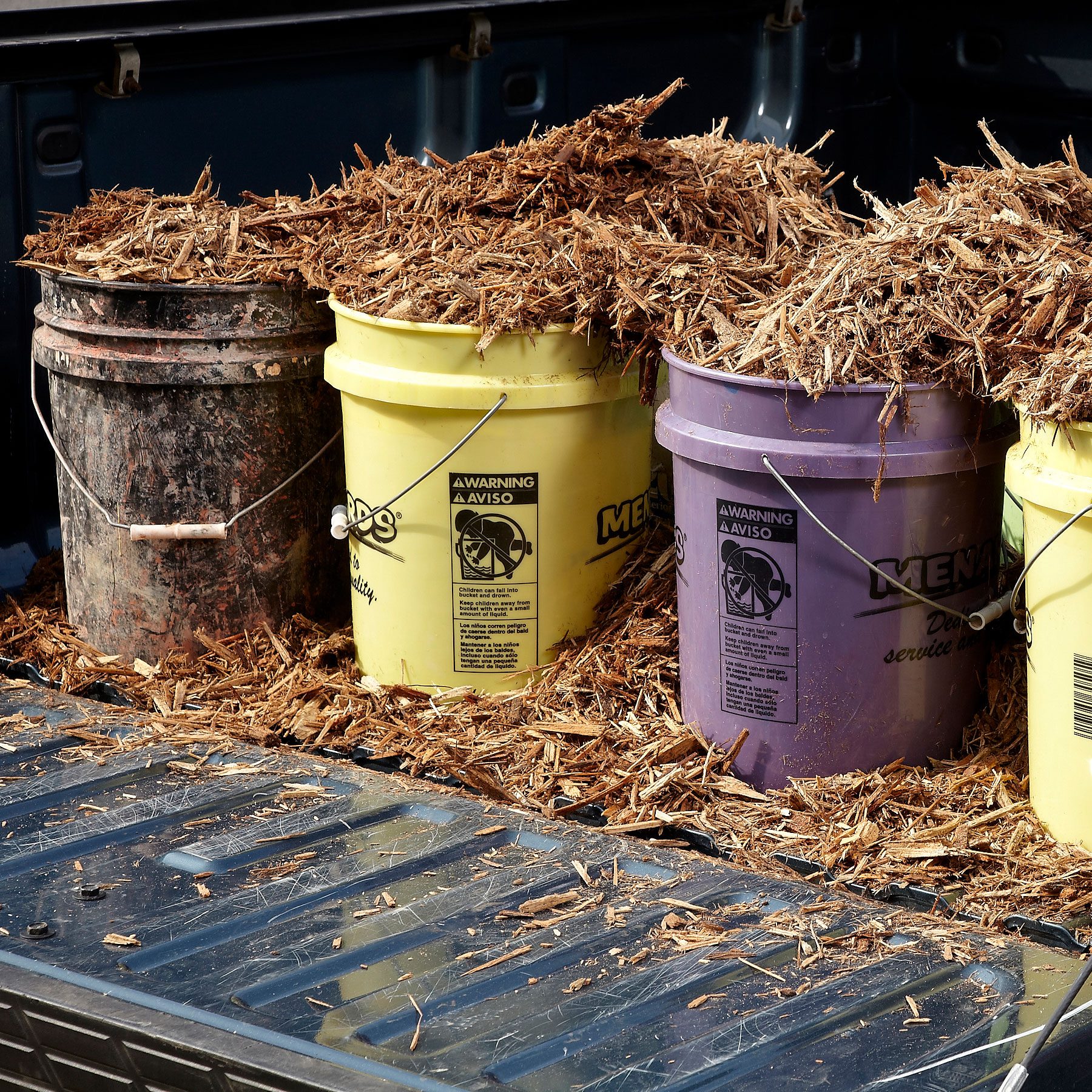 many 5 gallon buckets in the back of a pickup truck with the tail gate open; mulch in the buckets in the truck bed