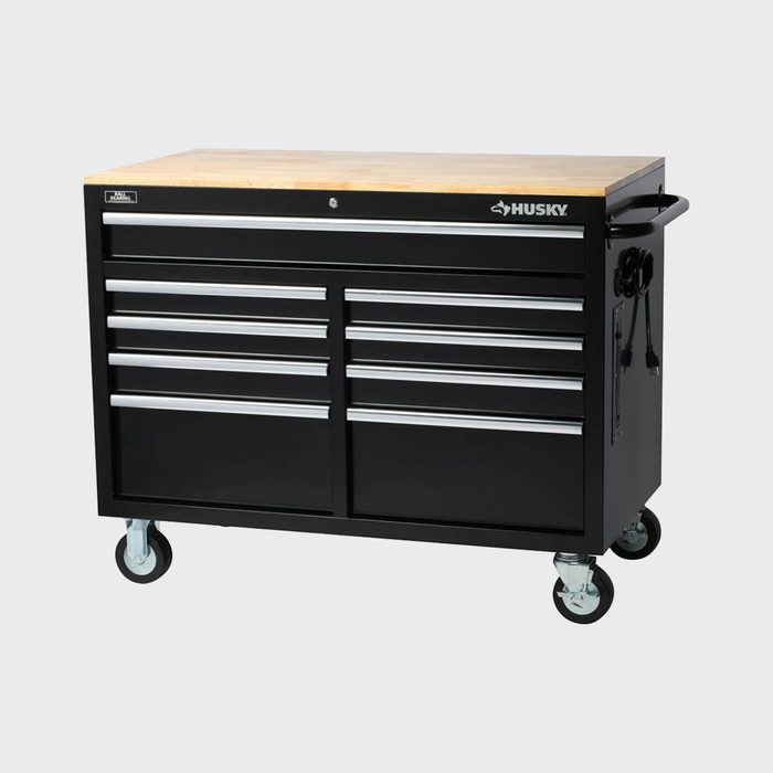A black tool cabinet with multiple drawers and a wooden top is positioned on wheels, designed for storage and organization in a workshop environment.