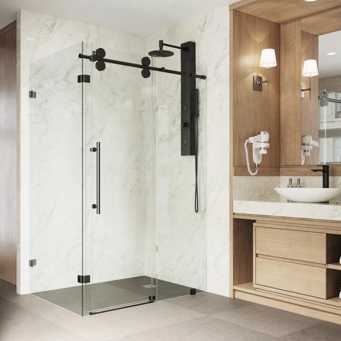 A glass shower with a black rainfall showerhead is situated in a modern bathroom, featuring marble walls and wooden cabinetry.